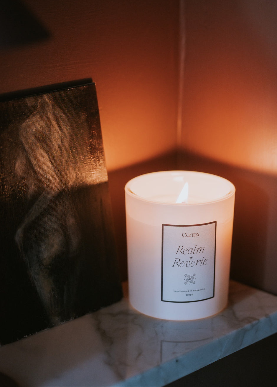 lit aromatherapy candle realm of reverie by Cerita on marble shelf with feminine artwork
