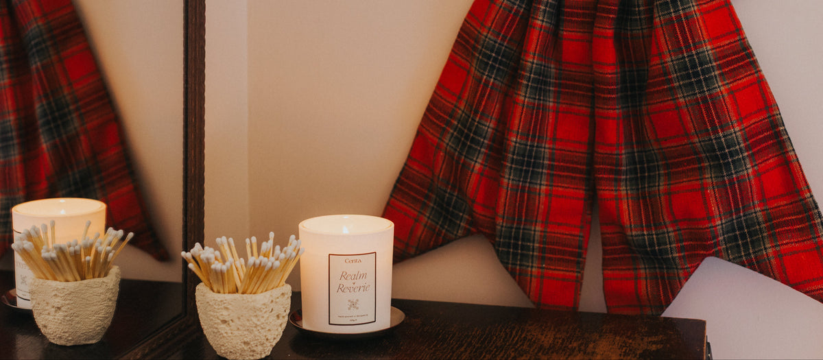 lit aromatherapy candles and pot of matches on wooden dresser with oversize red tartan bow in background