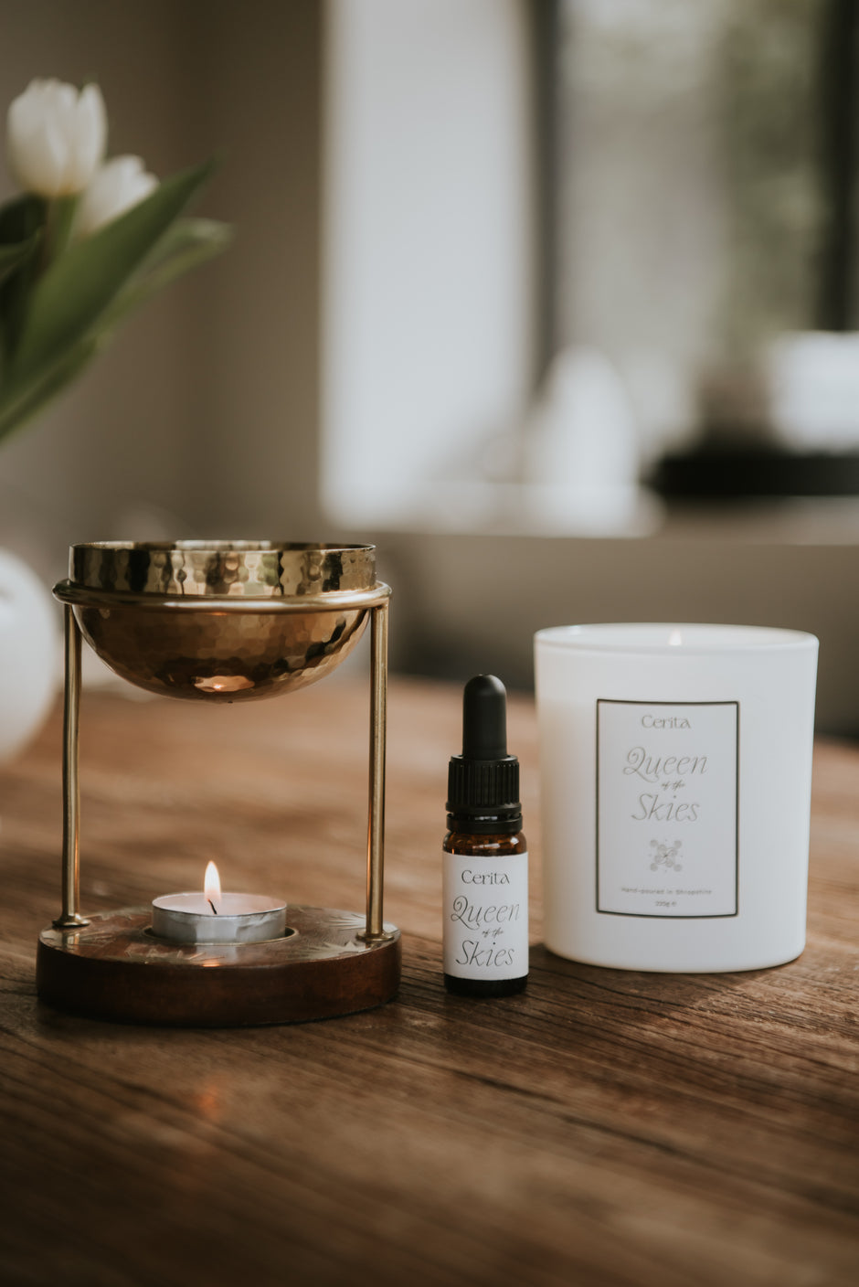 bottle of queen of the skies essential oil blend and aromatherapy candle by Cerita with lit oil burner in neutral interior setting