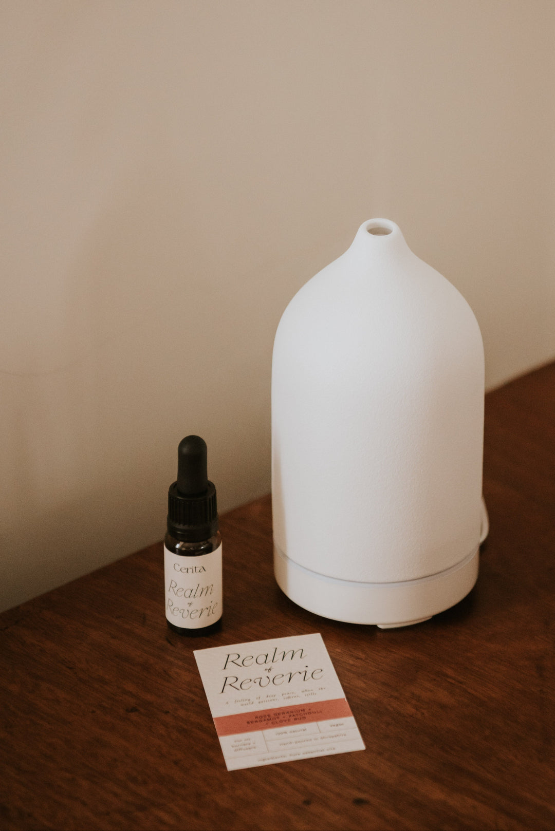 bottle of realm of reverie essential oil blend by Cerita next to white ceramic diffuser on wooden surface