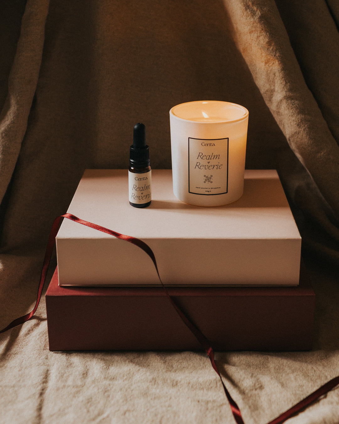 bottle of essential oil blend and lit aromatherapy candle on a stack of boxes with ribbon