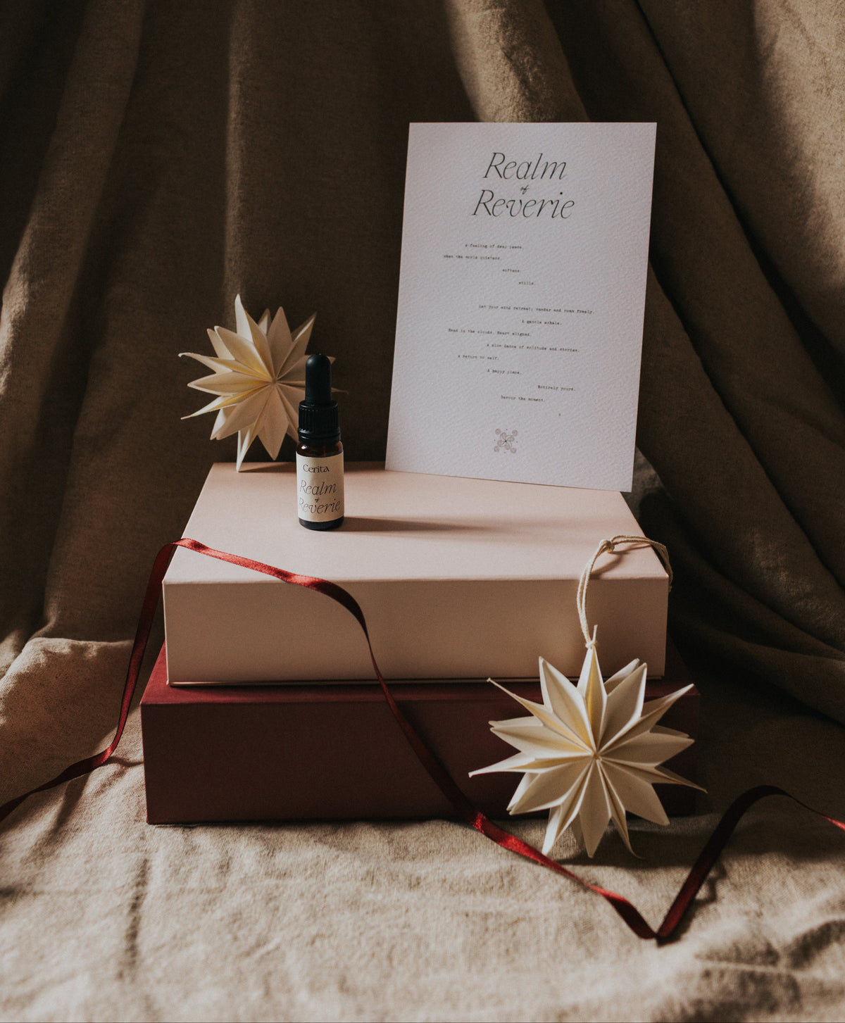 bottle of essential oil blend and typography art print on stacked gift boxes with draped ribbon and origami star decorations