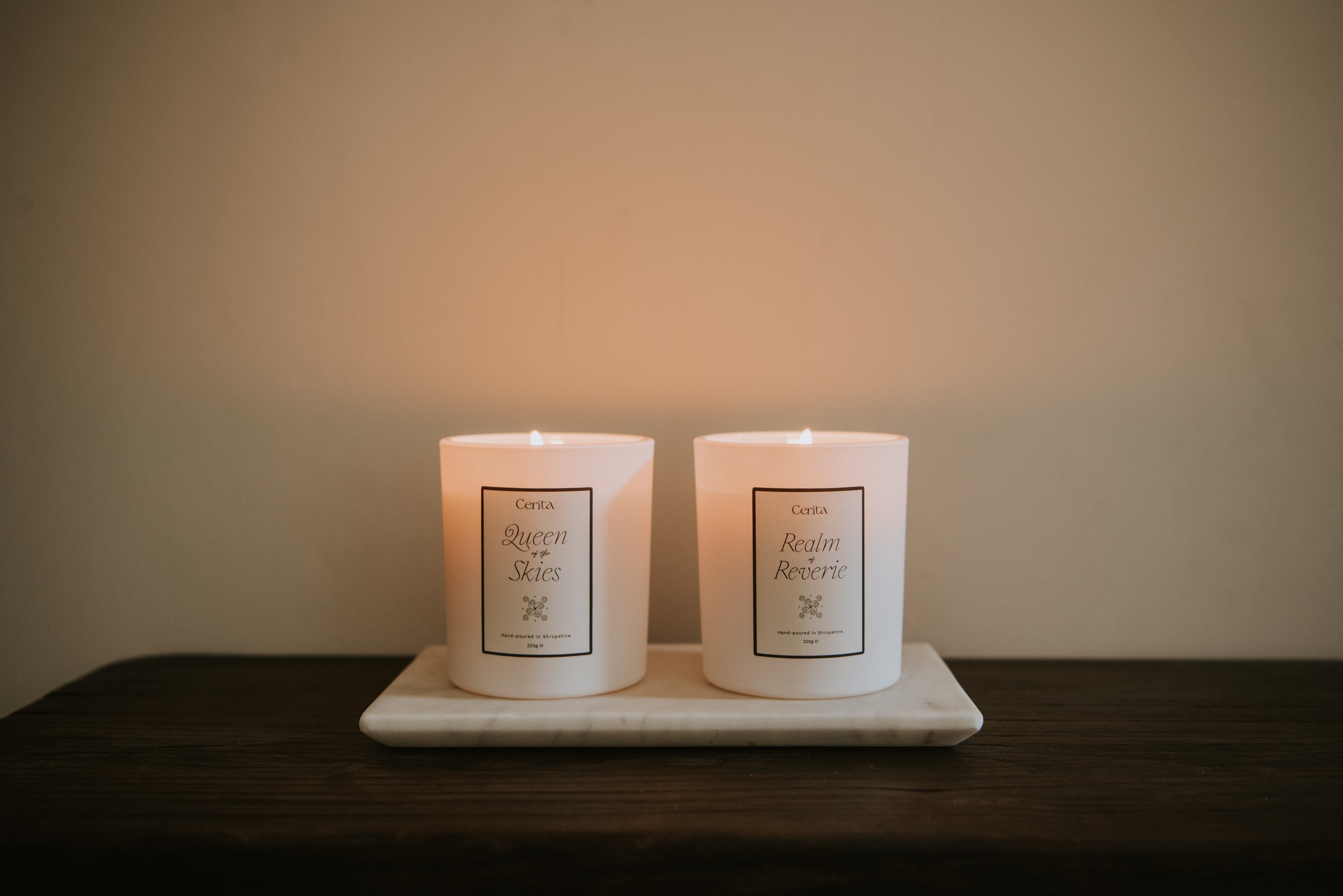 two lit aromatherapy candles in white vessels by Cerita on marble tray on wooden surface