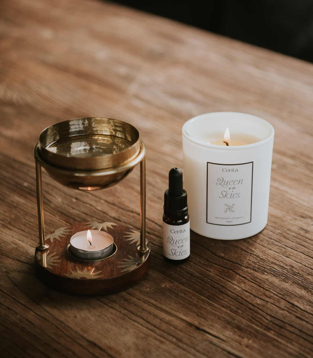 bottle of queen of the skies essential oil blend and aromatherapy candle by Cerita with oil burner on wooden table