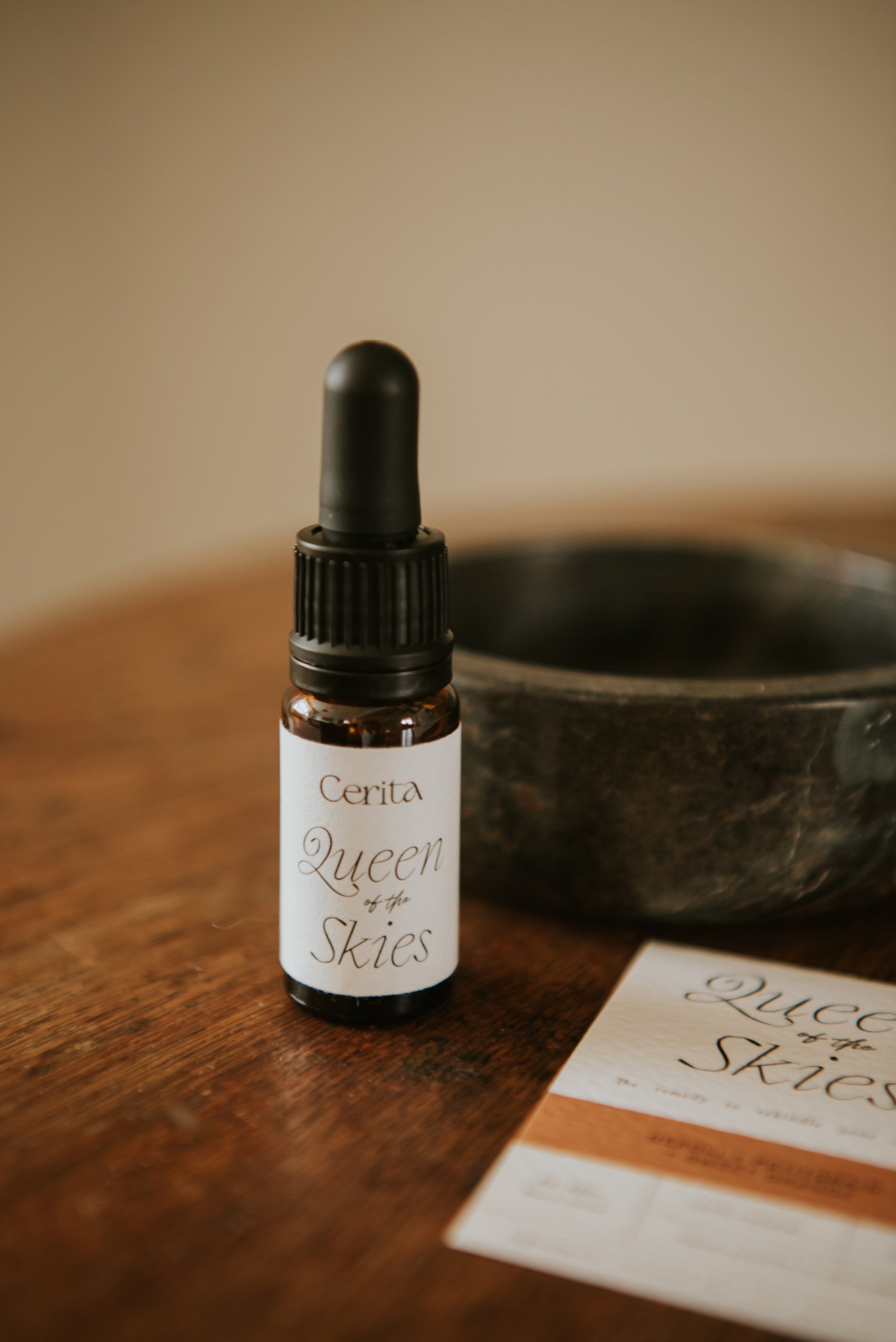 bottle of queen of the skies essential oil blend by Cerita on wooden surface with dark marble trinket bowl