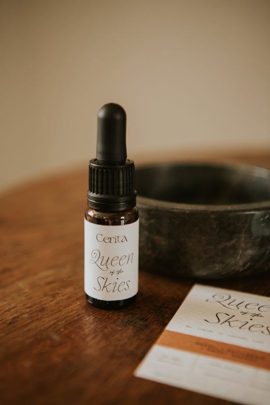 bottle of queen of the skies essential oil blend by Cerita on wooden surface with dark marble trinket bowl