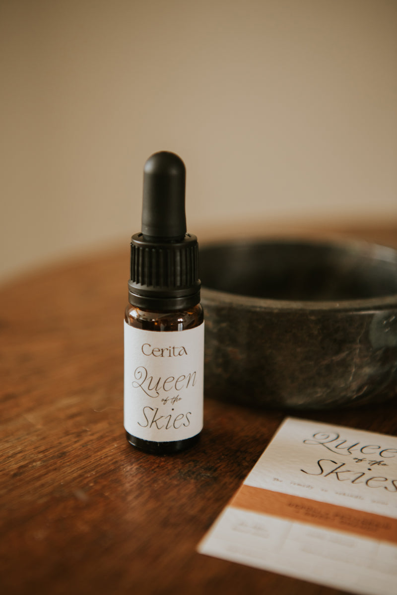 bottle of queen of the skies essential oil blend by Cerita on wooden surface with dark marble trinket bowl