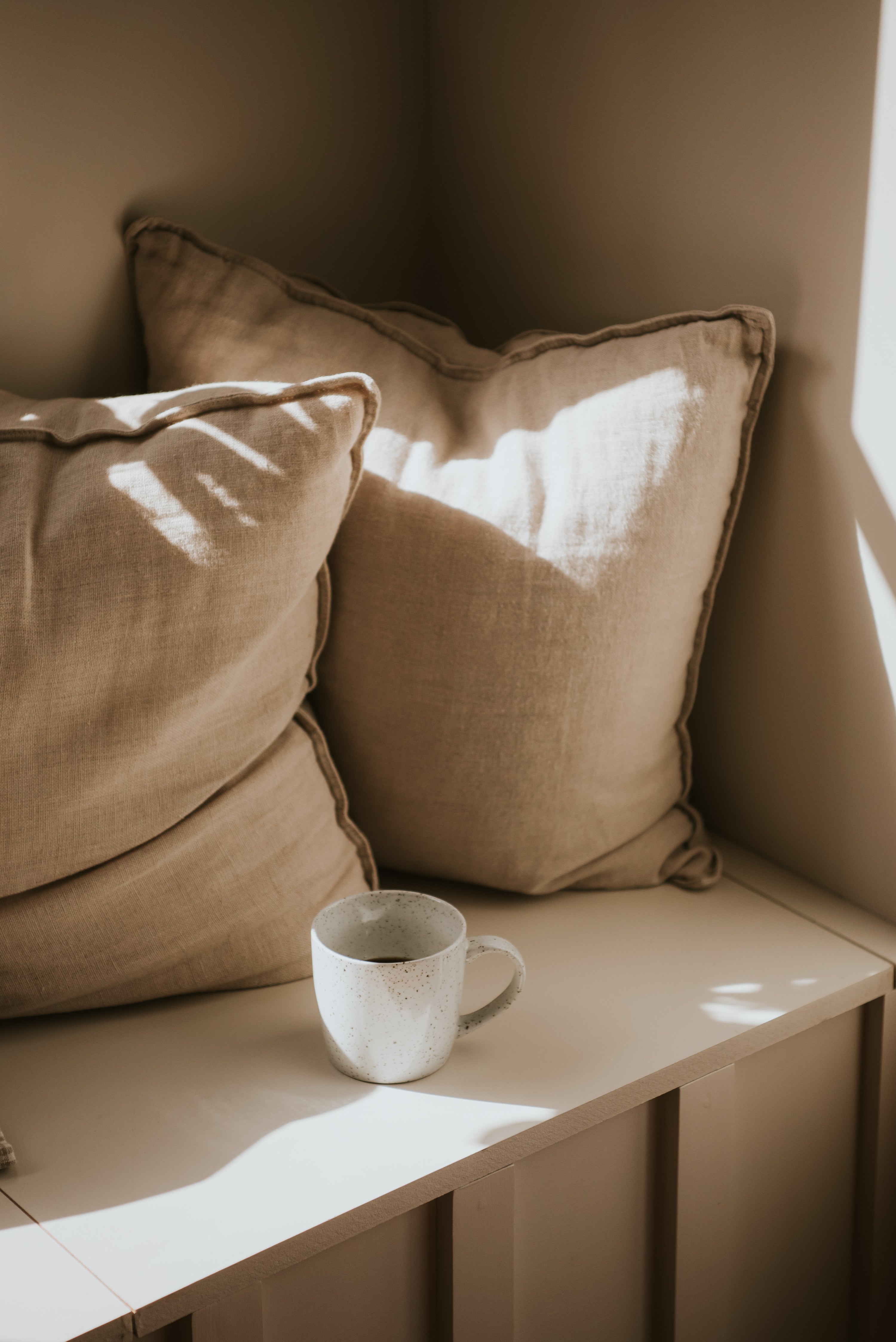 cup of coffee on bench with light and shadow in neutral interior setting 