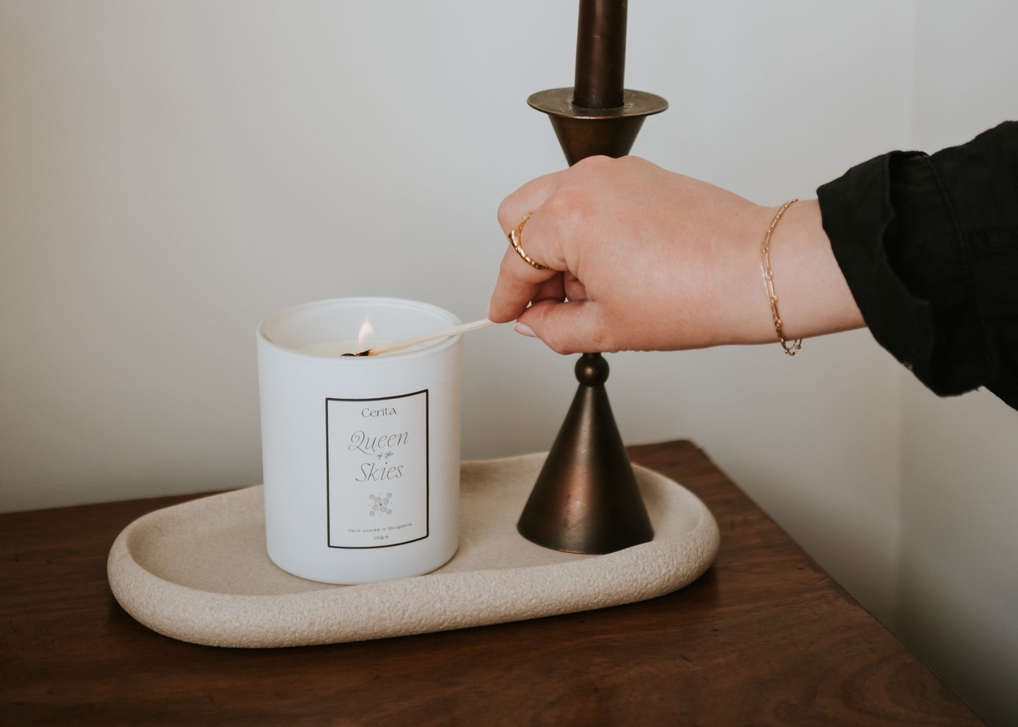 person lighting queen of the skies candle by Cerita on a neutral ceramic tray and wooden surface