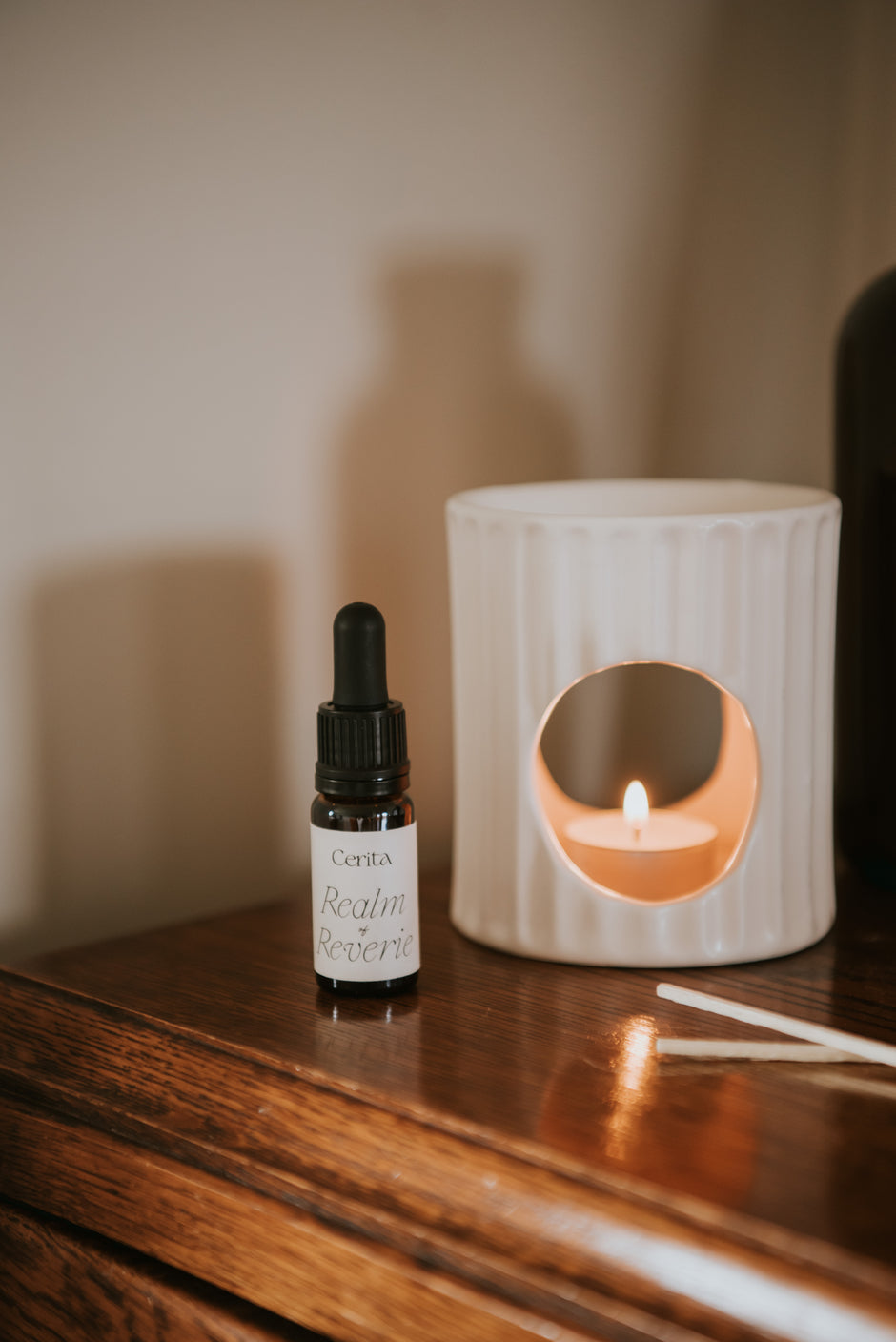 bottle of realm of reverie essential oil blend by Cerita with neutral lit oil burner on wooden dresser